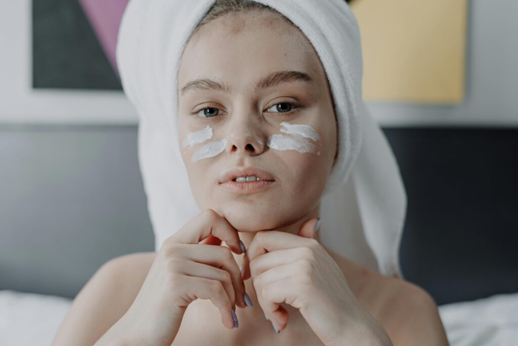 Portrait of a young woman with facial cream, wrapped in a towel, indoor setting.